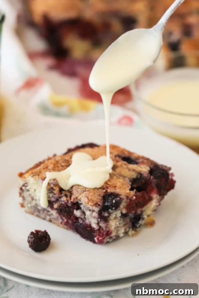 Mixed berry coffee cake on a white plate with vanilla glaze being poured over the top. The best breakfast cake recipe for berry lovers.