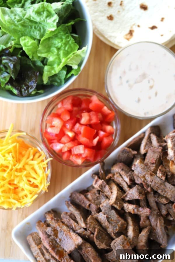 Chipotle Carne Asada recipe served on a cutting board with taco fixings like cheese, tomatoes, lettuce, and chipotle ranch for making delicious burritos and tacos.
