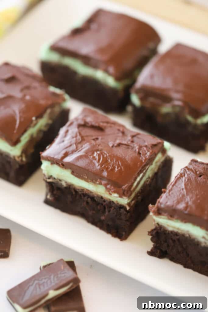 A serving plate full of Mint Chocolate brownies, with flavors of creme de menthe. There is a mint frosting layer and chocolate ganache layer on top.