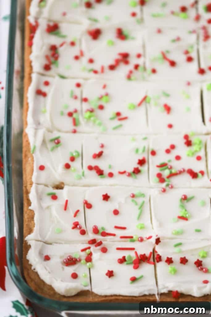 A festive tray of baked Christmas sugar cookie bars, generously topped with smooth buttercream frosting and a colorful array of holiday sprinkles, ready to be served.