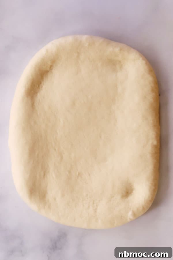 White bread dough neatly rolled out into a perfect rectangle on a lightly floured surface, ready for shaping into loaves.