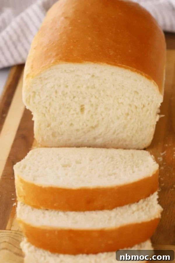 A freshly baked loaf of homemade white bread on a wooden cutting board being sliced, revealing its soft and airy interior, ready for serving.