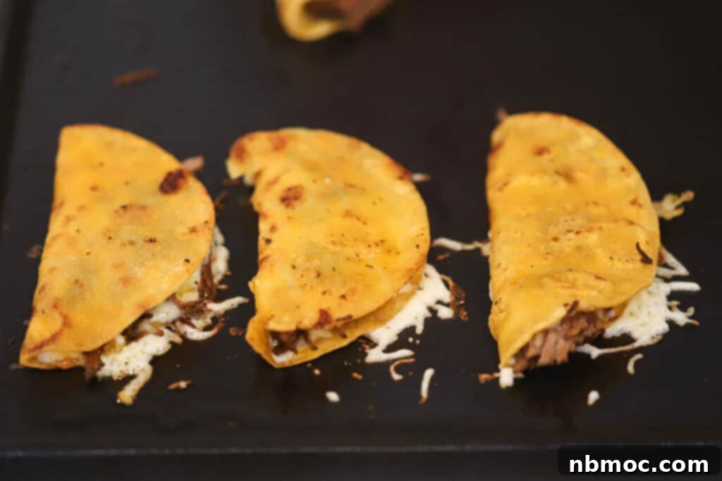 Birria tacos on a hot skillet being cooked until crispy.