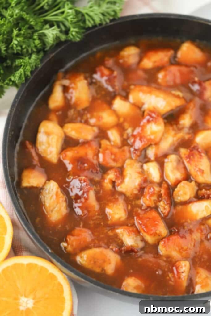 A skillet full of homemade orange chicken, with bite sized pieces of chicken coated in a crispy batter and covered in a flavorful sticky orange chicken sauce.