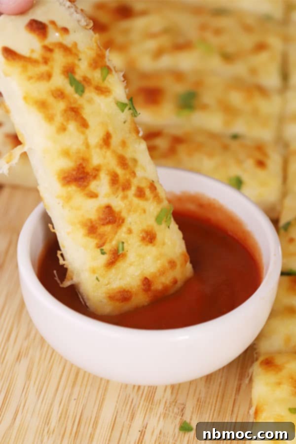 Homemade cheesy breadsticks being dipped into a bowl of marinara sauce, showcasing their appeal.