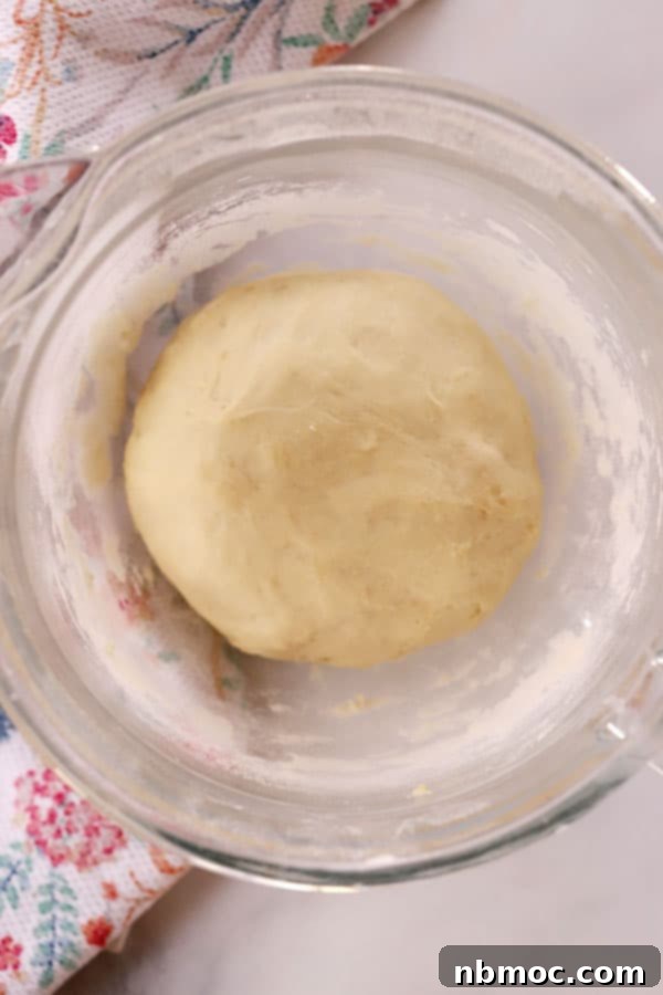 A smooth, risen ball of yeast dough resting in a glass bowl, prepared for making homemade breadsticks.