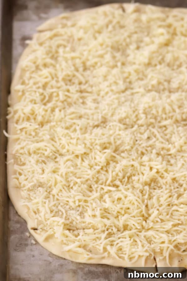 Unbaked cheesy breadsticks topped with shredded mozzarella cheese on a baking sheet, ready for the oven.