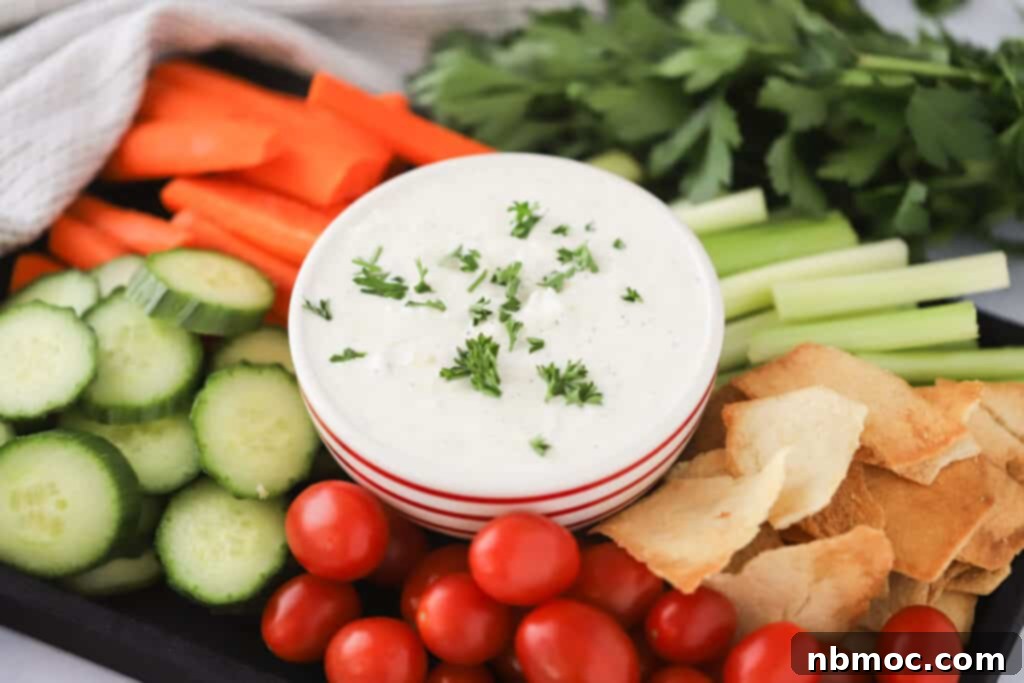 The Ultimate Refreshing Greek Yogurt Dip 3 Easy Homemade Tzatziki recipe, garnished with fresh herbs, served on a rustic wooden board alongside a colorful array of fresh vegetables and crispy pita chips for dipping.