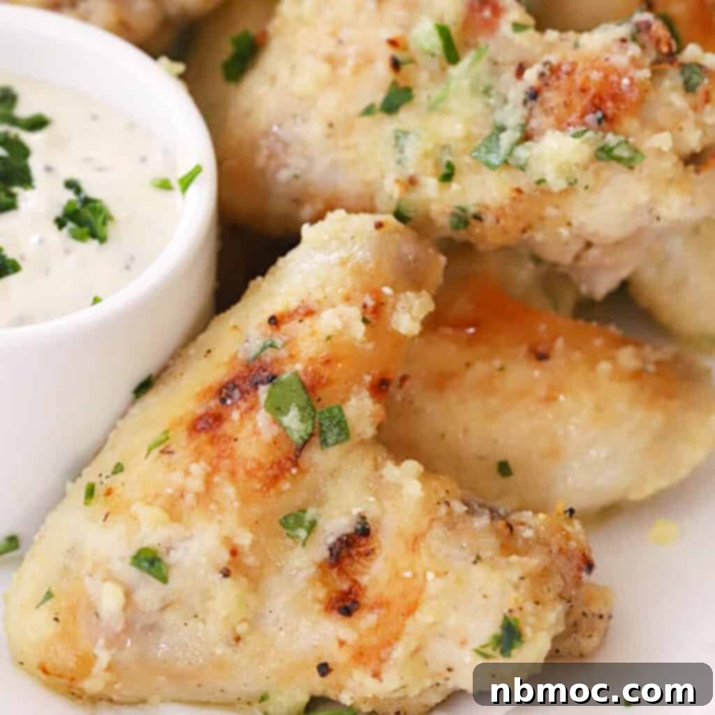 Baked Garlic Parmesan chicken wings on a serving platter with a side bowl of dipping sauce, garlic parmesan wings recipe. Garlic parmesan chicken wings for a Taylor Swift party.