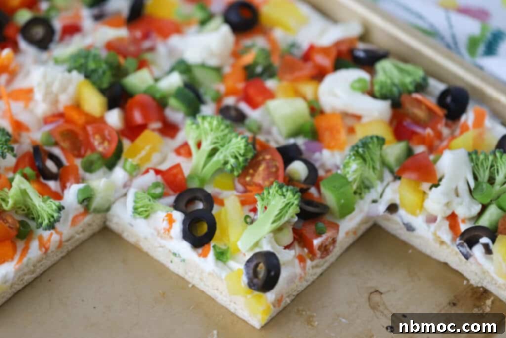 A sheet tray of crescent dough veggie pizza, topped with ranch cream cheese and veggies.