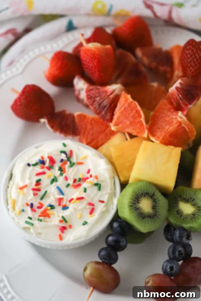 rainbow fruit kebabs on a serving plate with a side of cream cheese fruit dip.