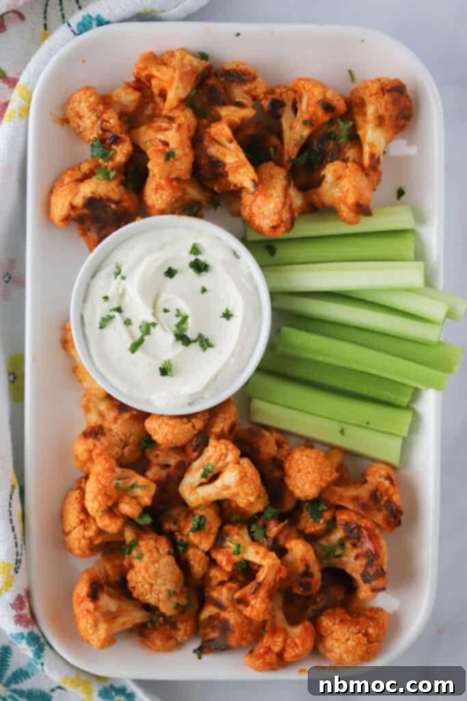 Roasted buffalo cauliflower bites on a serving platter with ranch dip and celery sticks, ready for a game day party.