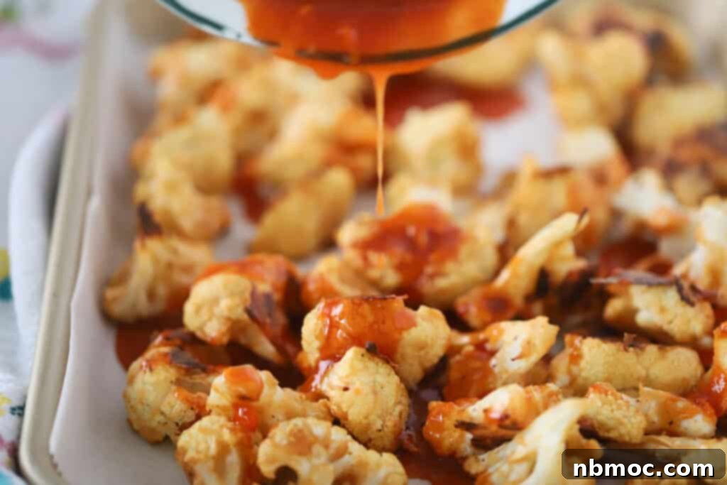 Homemade buffalo sauce being poured over roasted cauliflower florets on a baking sheet for ultimate flavor.