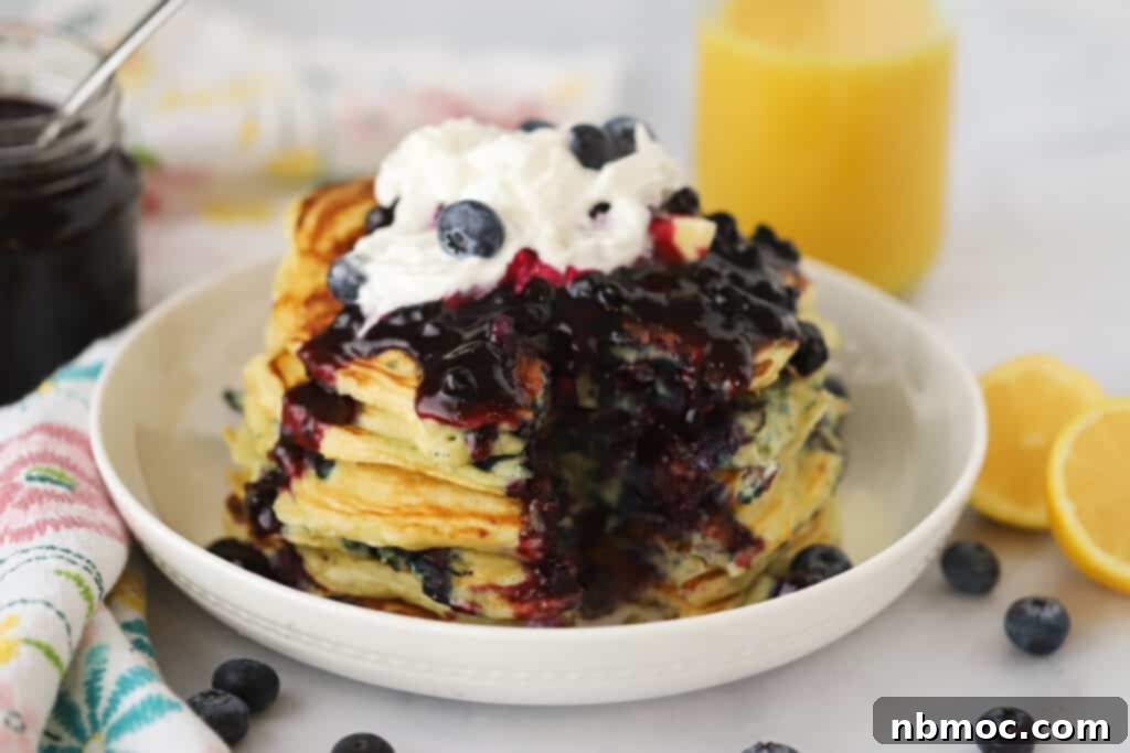 Homemade blueberry syrup poured over a stack of pancakes with whipped cream.