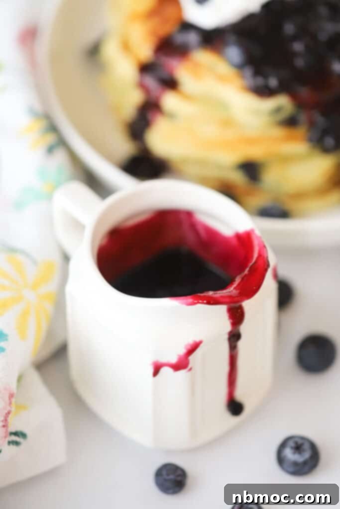 Blueberry syrup in a ramekin being served with breakfast pancakes and waffles.