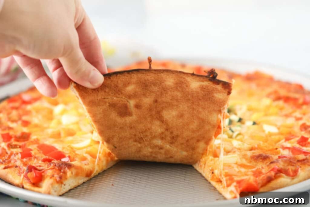 Garden Harvest Pizza 4 A hand grabbing a slice of baked veggie pizza.