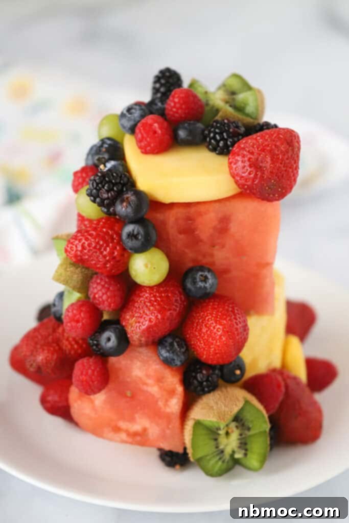 A Fresh Fruit Cake made with watermelon, pineapple, berries, kiwi, and mango on a serving plate, adorned with mint leaves.