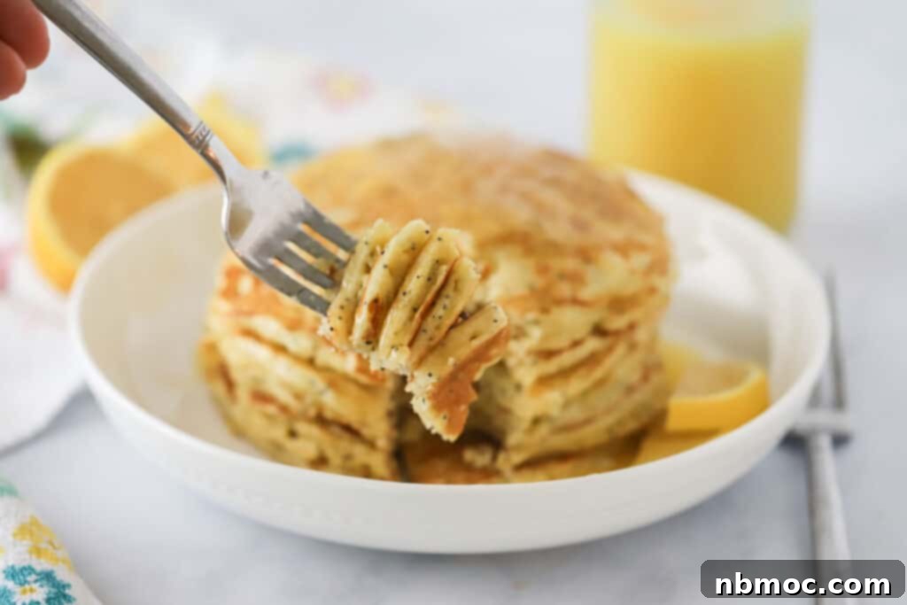 Sunny Lemon Poppy Seed Pancakes 5 A fork digging into a stack of fluffy lemon poppy seed pancakes, drizzled with sweet maple syrup, highlighting the delicious texture.