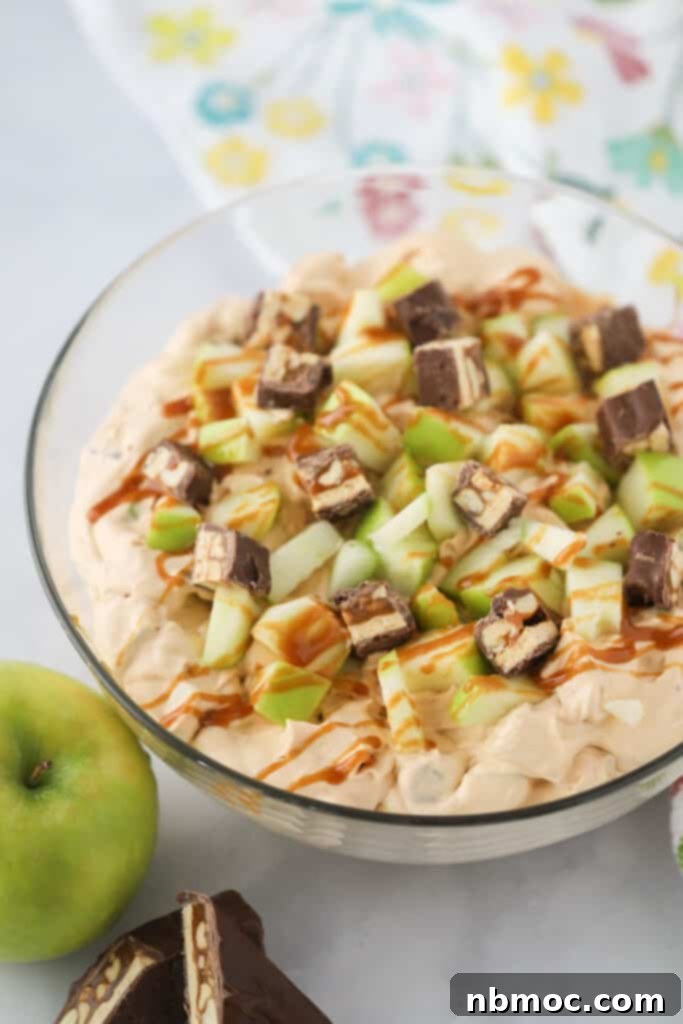 A large bowl full of Snickers Apple Salad topped with caramel sauce, Granny smith apples, and bite sized Snickers candy bars.