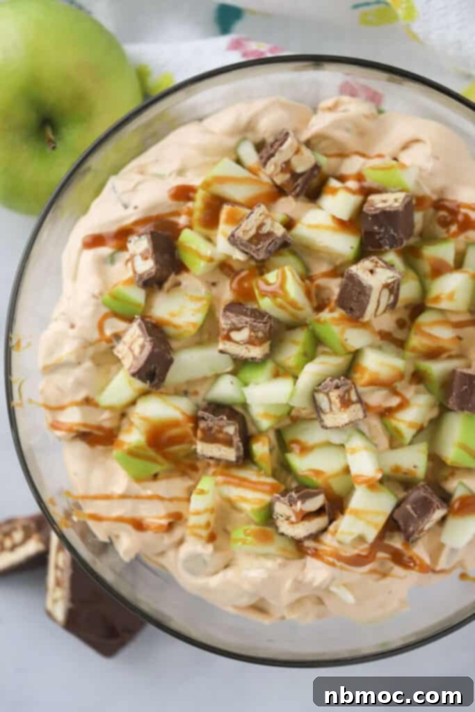 Apple salad with Snickers in a large bowl topped with caramel sauce.