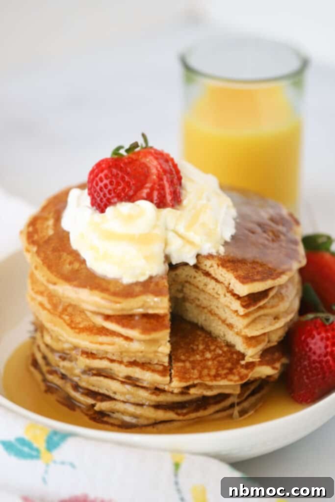 A beautifully arranged stack of whole wheat pancakes, generously drizzled with syrup and adorned with whipped cream and a scattering of fresh berries.