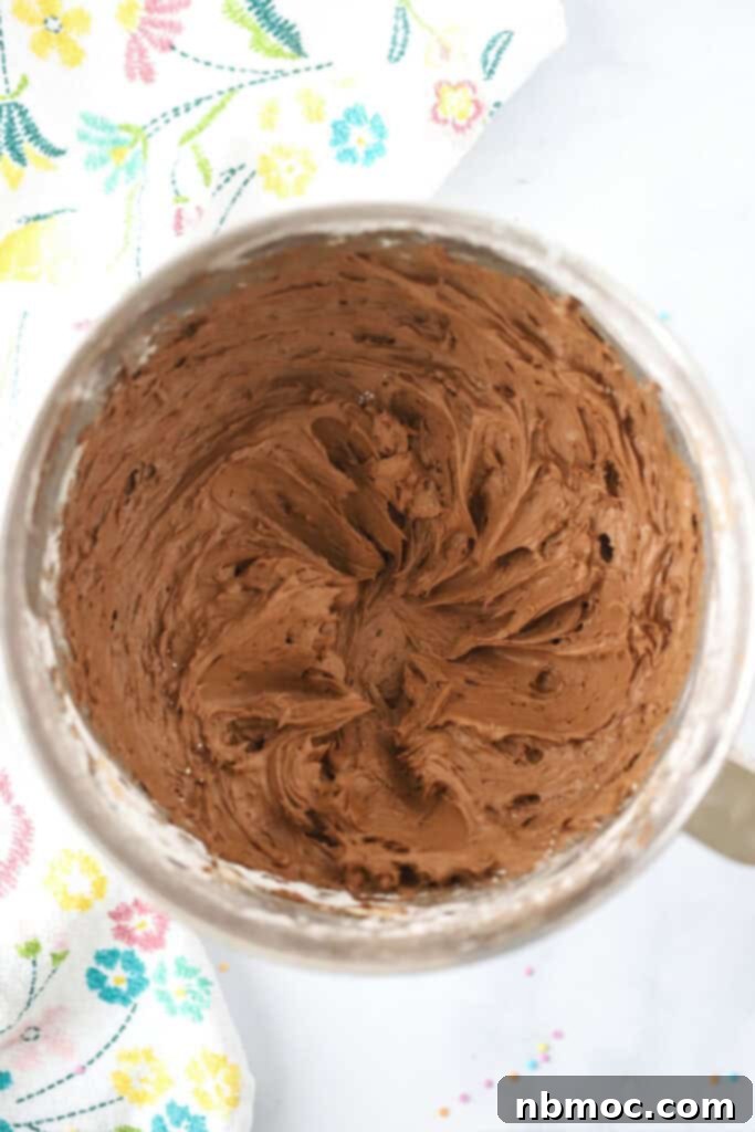 Luscious Chocolate Cream Cheese Frosting 4 A charming wooden bowl filled to the brim with smooth, rich chocolate cream cheese frosting rests on a rustic wooden tabletop, ready for use.