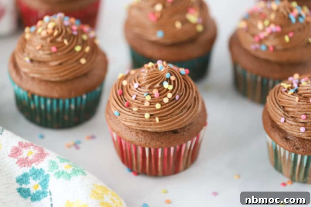 Luscious Chocolate Cream Cheese Frosting 5 A beautifully arranged table showcasing chocolate cupcakes generously decorated with piped chocolate cream cheese frosting, adorned with a scattering of colorful sprinkles.