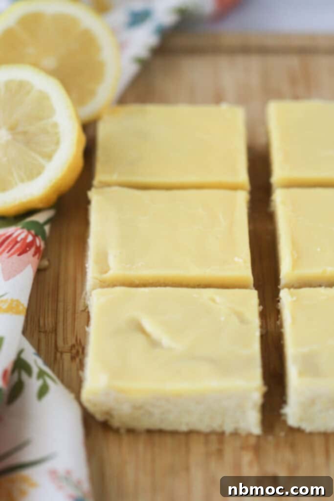 A wooden cutting board displaying perfectly cut squares of luscious lemon fudge blondies, each topped with a delicate layer of lemon icing.