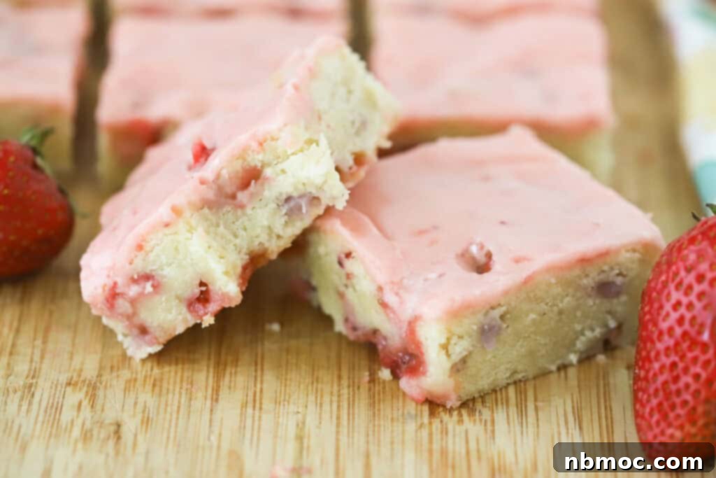 Squares of strawberry lemon blondies topped with pink strawberry icing on a countertop.