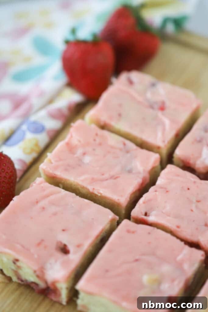 Strawberry blondie squares on a cutting board topped with pink icing.