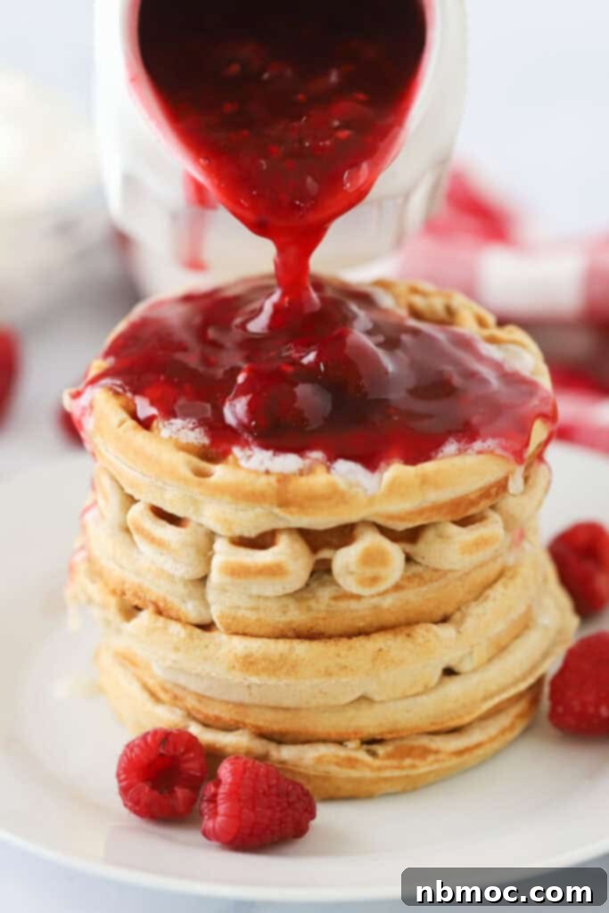 A stack of fluffy waffles with rich raspberry syrup being poured over the top, ready to be enjoyed.