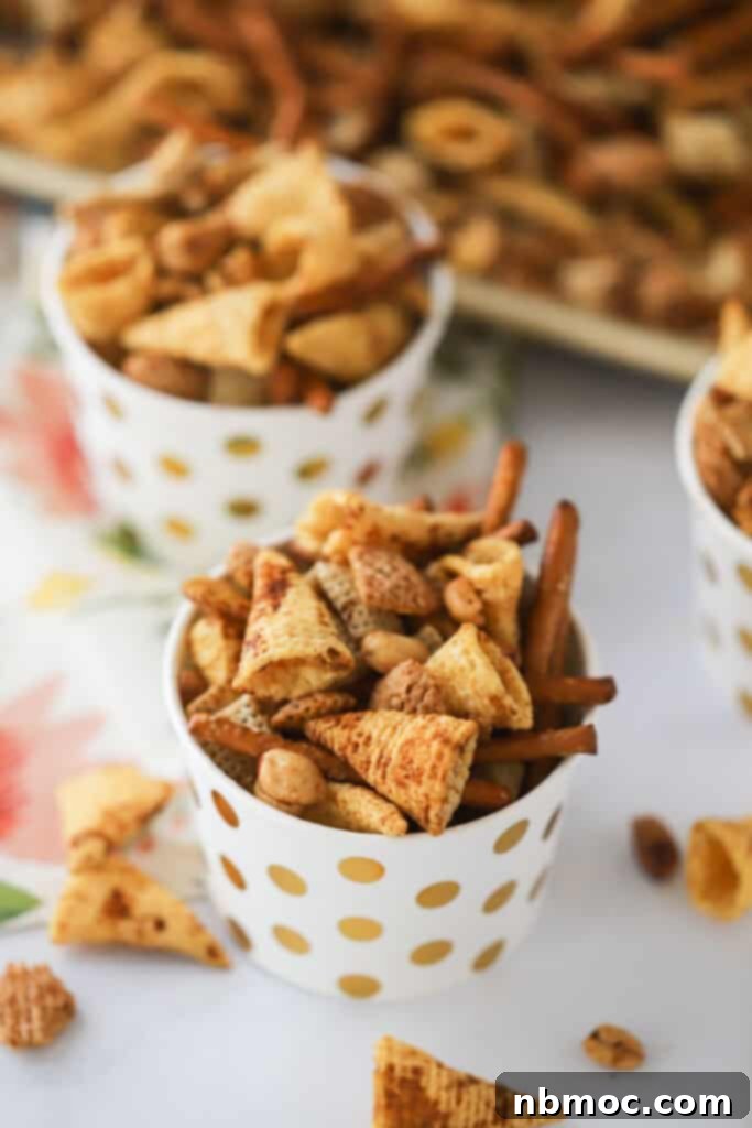 Small decorative cups brimming with perfectly baked homemade Chex Party Mix, featuring a tempting mix of crispy cereals, pretzels, and nuts.