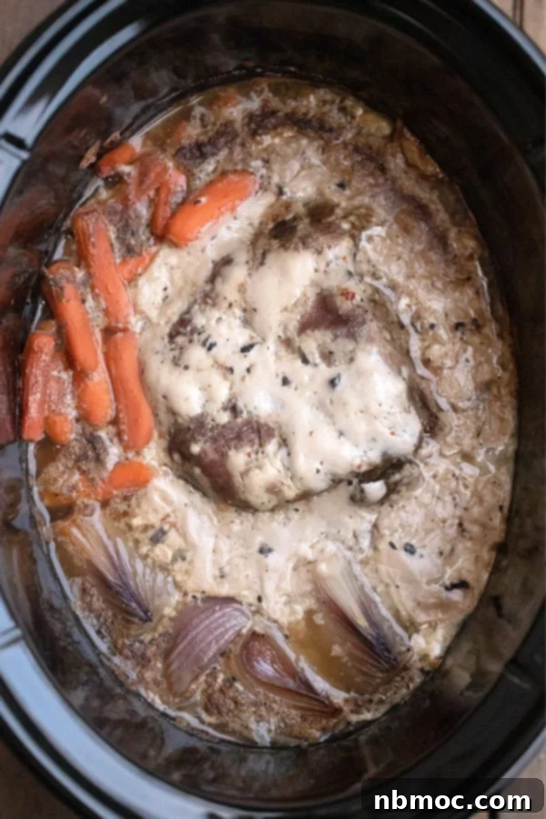 Close-up of crock pot venison roast cooking with carrots and onions, showcasing the rich broth.