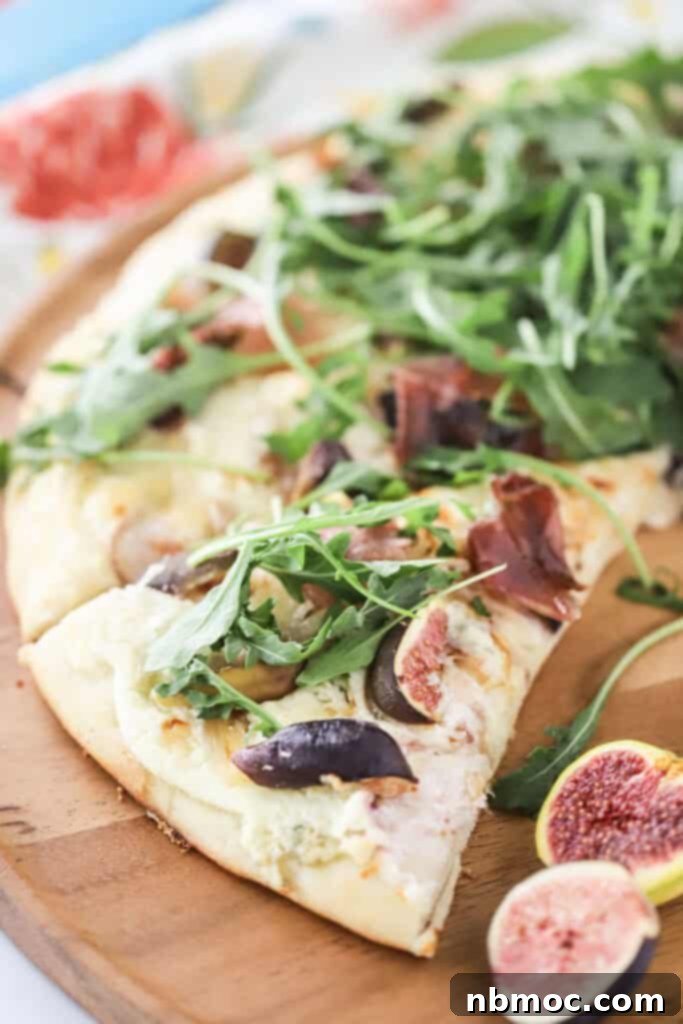 A cutting board with slices of fig and prosciutto pizza topped with fresh arugula.