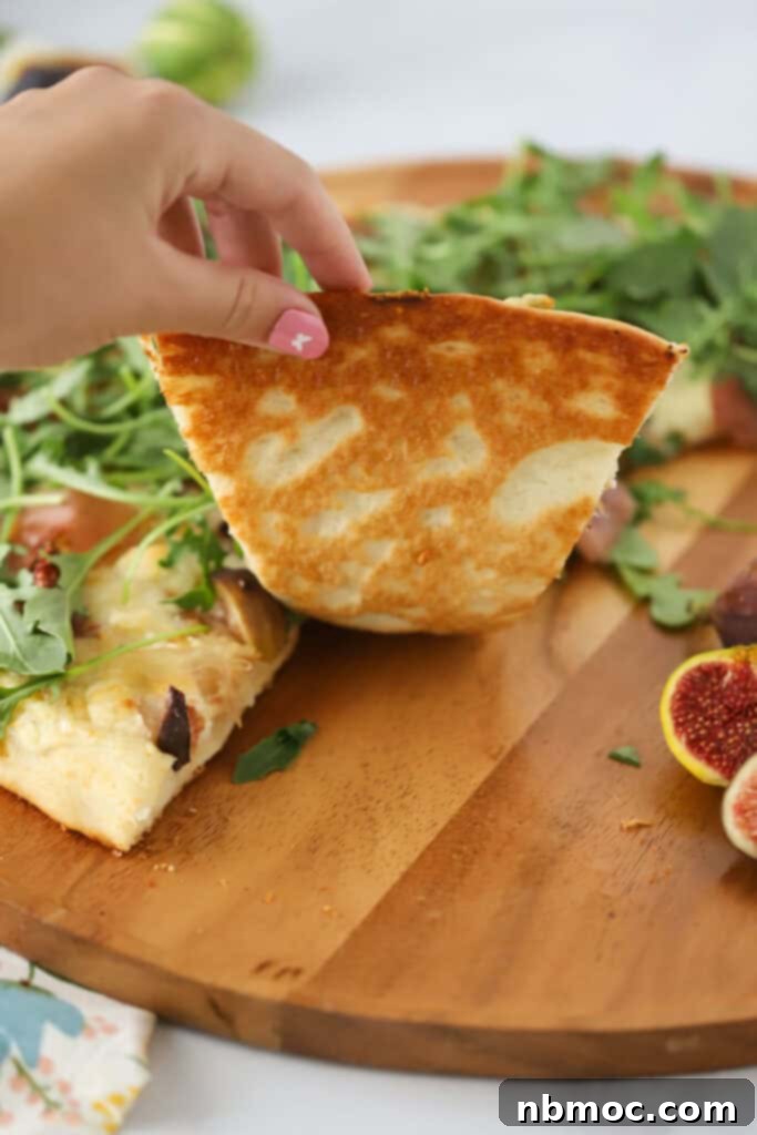 A hand grabbing a slice of prosciutto and fig pizza.