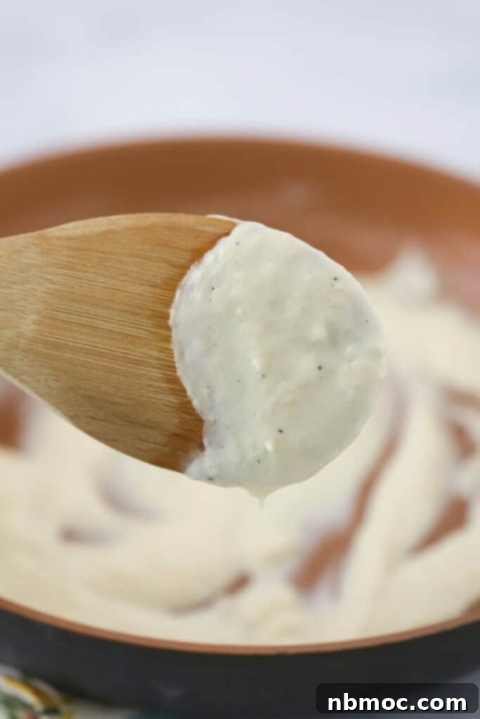 Creamy White Pizza Sauce 2 A bowl with white pizza sauce and a wooden spoon coated in the sauce.
