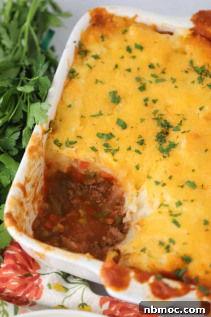 A large baking dish full of shepherd's pie, with a generous portion already served, revealing the layers of mashed potatoes and beef filling.