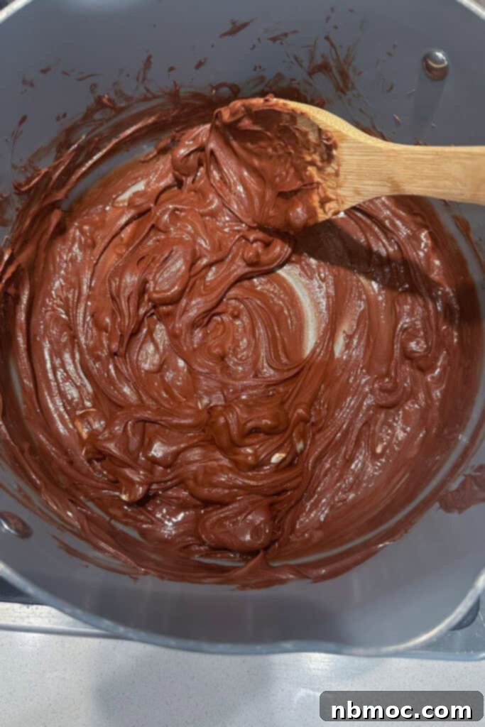 A large bowl full of melted chocolate and peanut butter with a wooden spoon, ready to coat the cereal.
