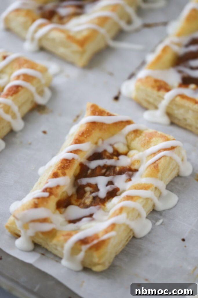 A baking sheet filled with golden brown Pumpkin Cream Cheese Danish, each glistening with a homemade vanilla glaze, ready to be enjoyed.