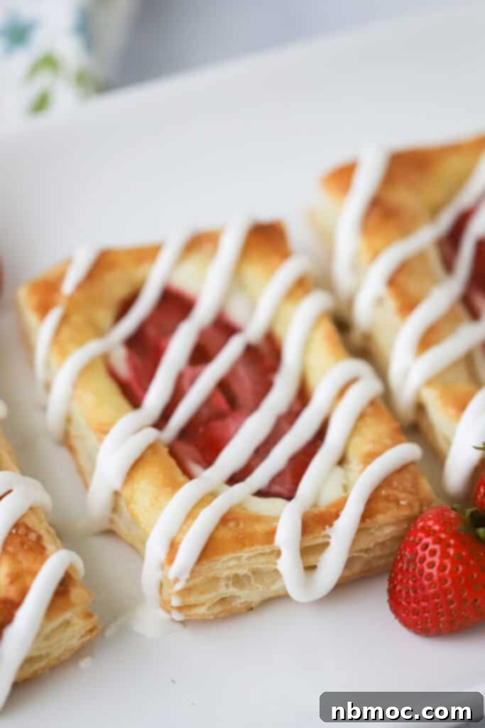 Flaky Strawberry Cream Cheese Delight 2 A white serving platter with strawberry danishes topped with glaze.