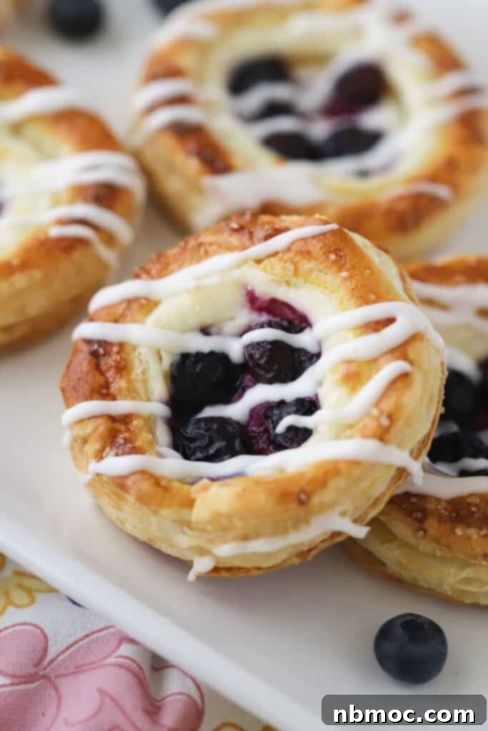 A plate full of golden brown blueberry danish pastries topped with a generous drizzle of homemade glaze.
