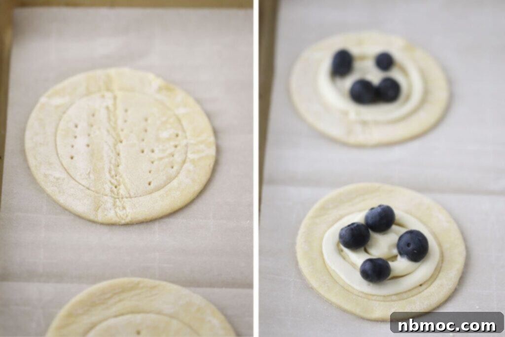 Puff pastry dough cut into circles with cream cheese filling and fresh blueberries over the top, ready for baking.