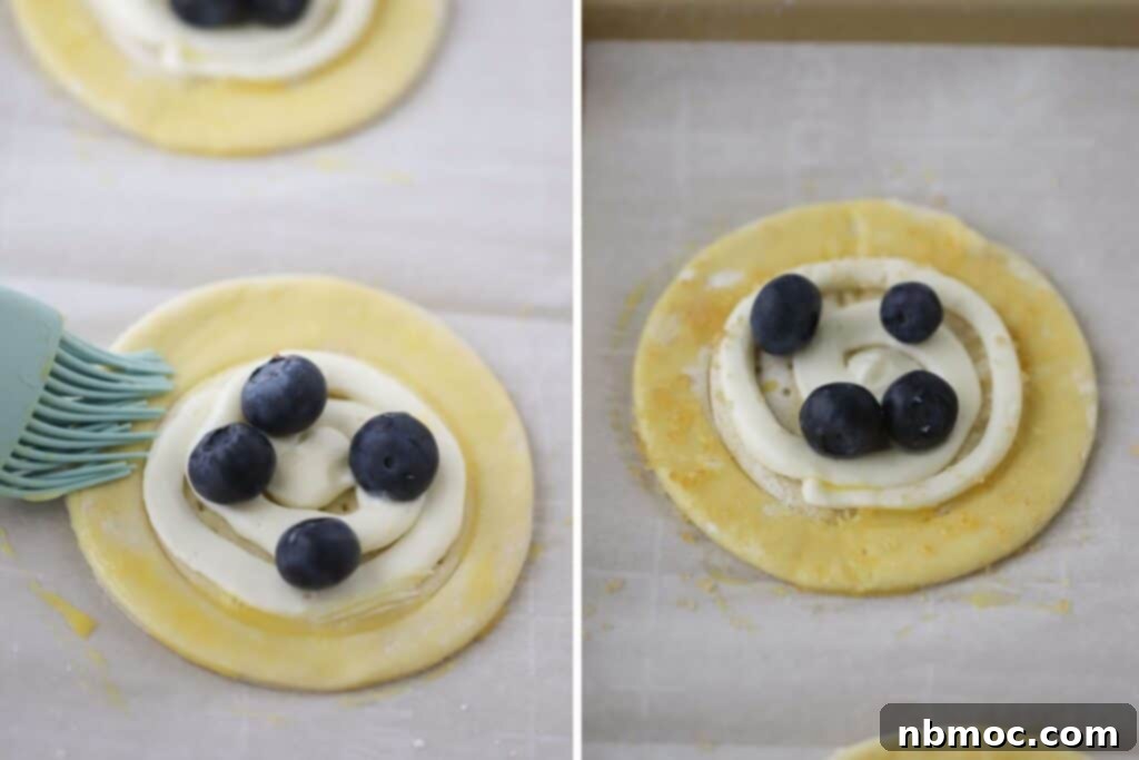 A hand brushing Danish puff pastry dough with egg wash just before placing it in the oven.