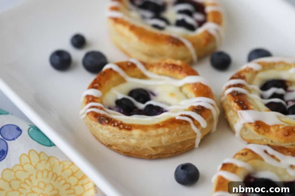 A white plate with freshly baked Blueberry Cheese Danish topped with a delicate drizzle of glaze, ready to be enjoyed.