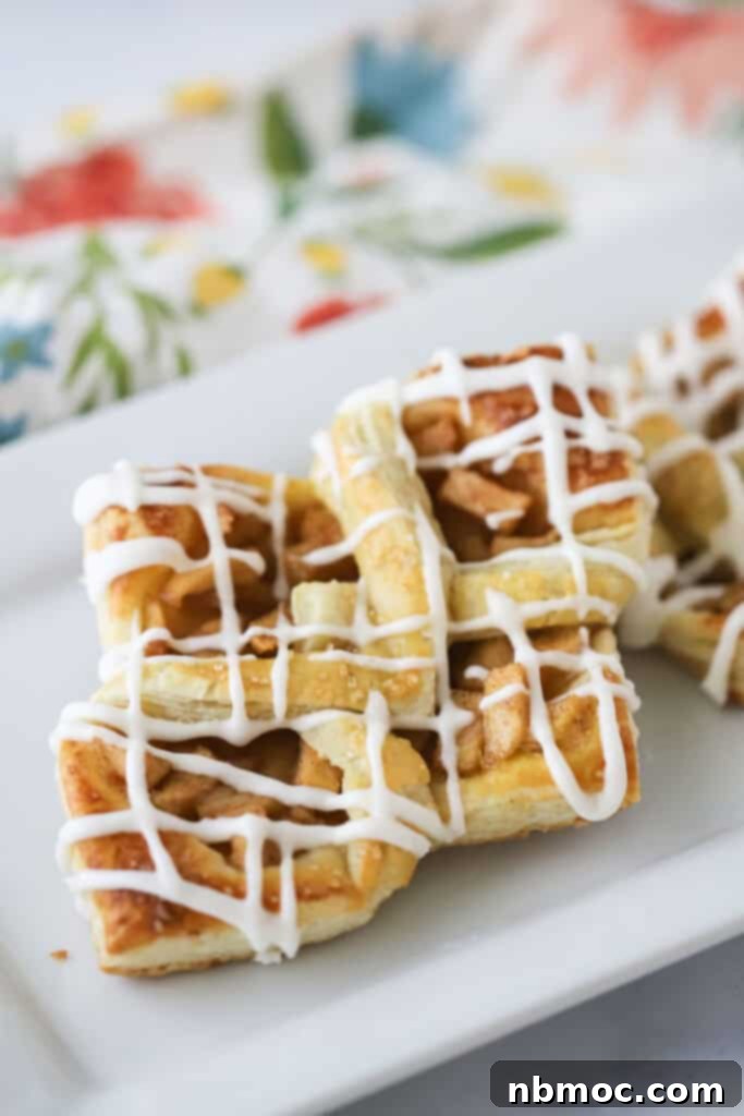 A plate full of golden-brown apple danish pastries made with flaky puff pastry, generously drizzled with a sweet white glaze.
