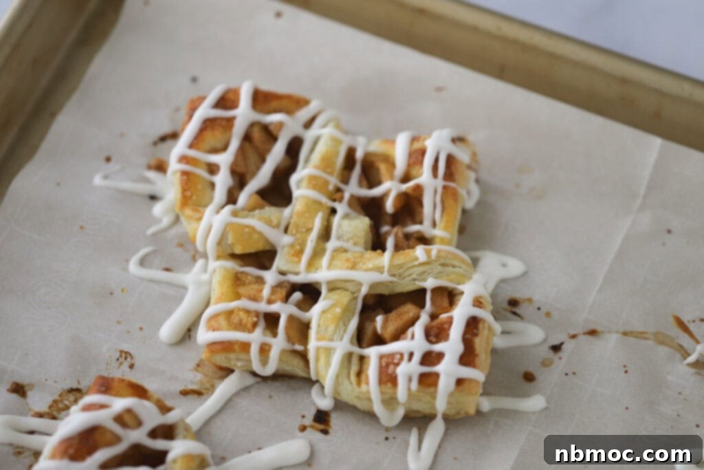A parchment-lined baking sheet showcasing freshly baked apple danish pastries, glistening with a sweet drizzle of glaze.