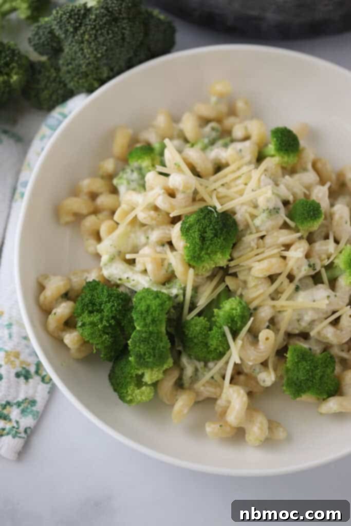 A white serving bowl full of creamy broccoli pasta, topped with shredded Parmesan cheese and fresh parsley.