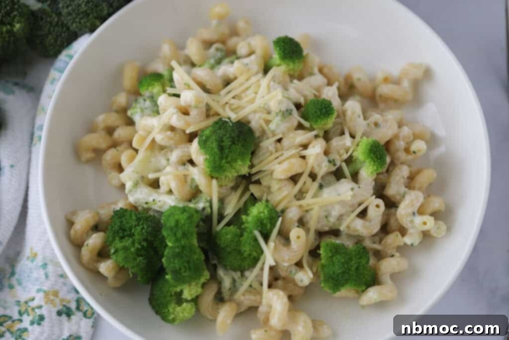 A white bowl filled with cavatappi pasta, creamy sauce, and broccoli, garnished with fresh herbs.