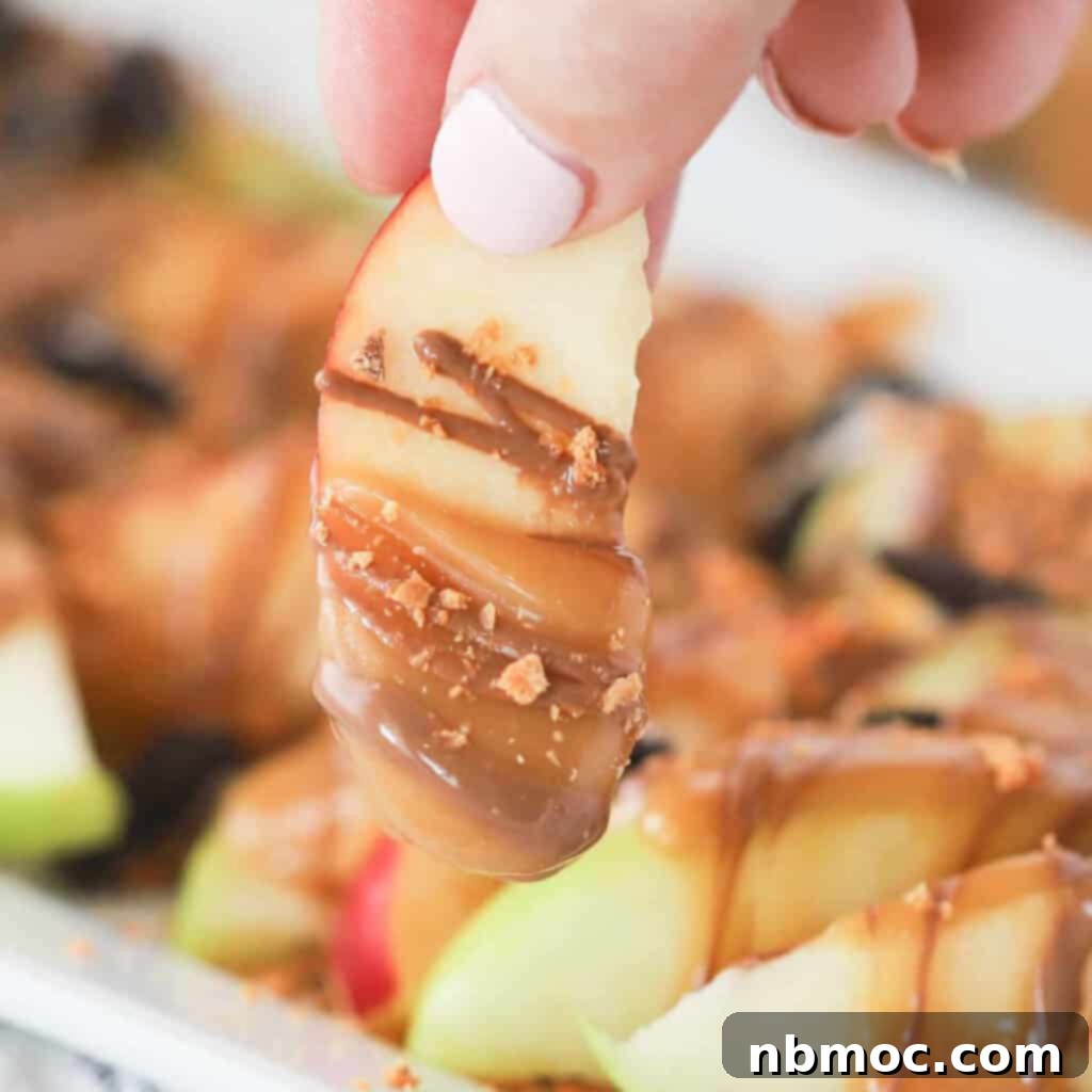 A hand gently dipping crisp apple slices into a luscious caramel sauce, highlighting the preparation of delicious apple nachos.