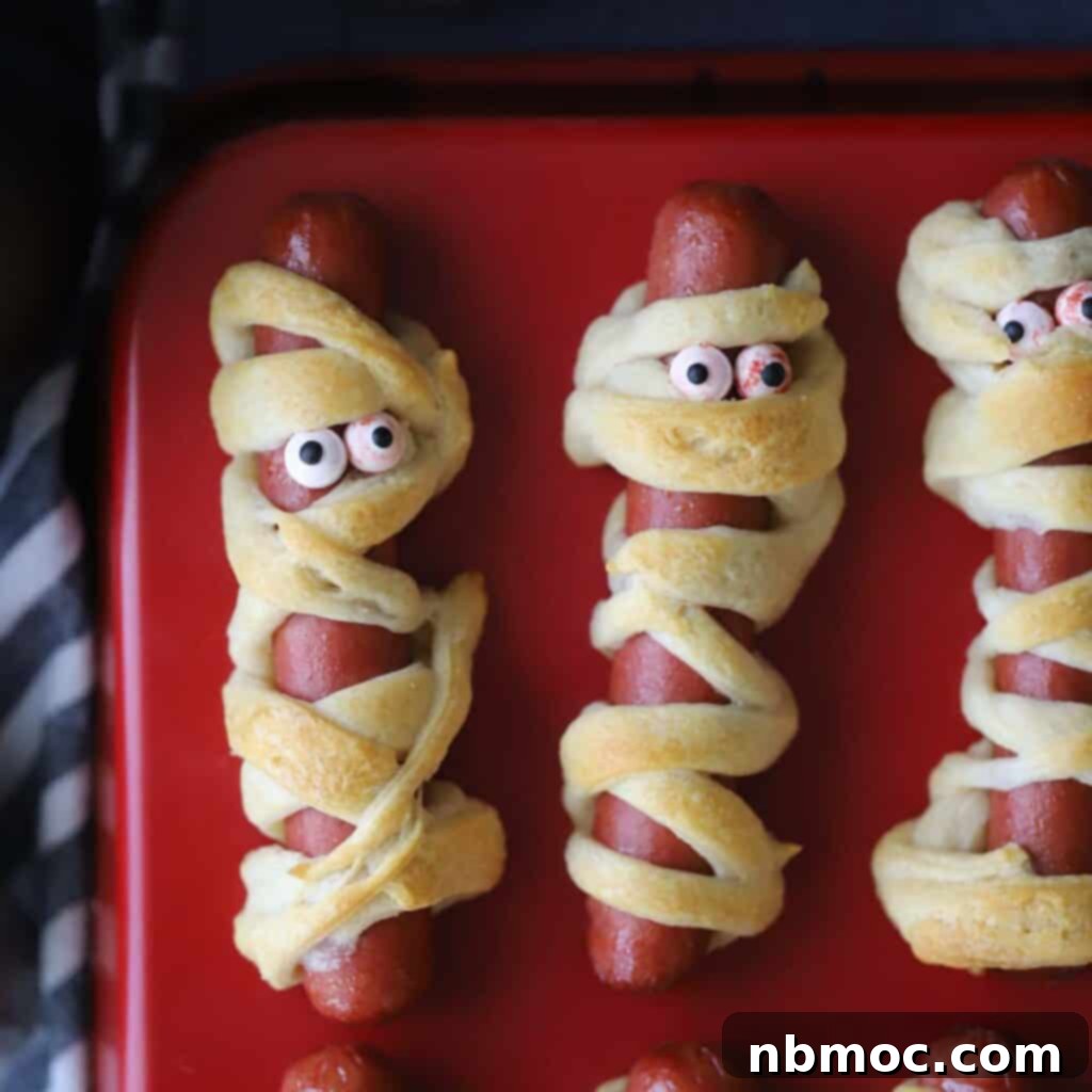 Adorable mummy hot dogs with playful candy eyes, arranged on a vibrant red serving tray, perfectly embodying the spirit of a fun Halloween feast.